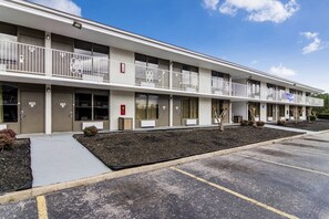 A multi-story motel with individual rooms, a parking lot, and a small landscaped area.