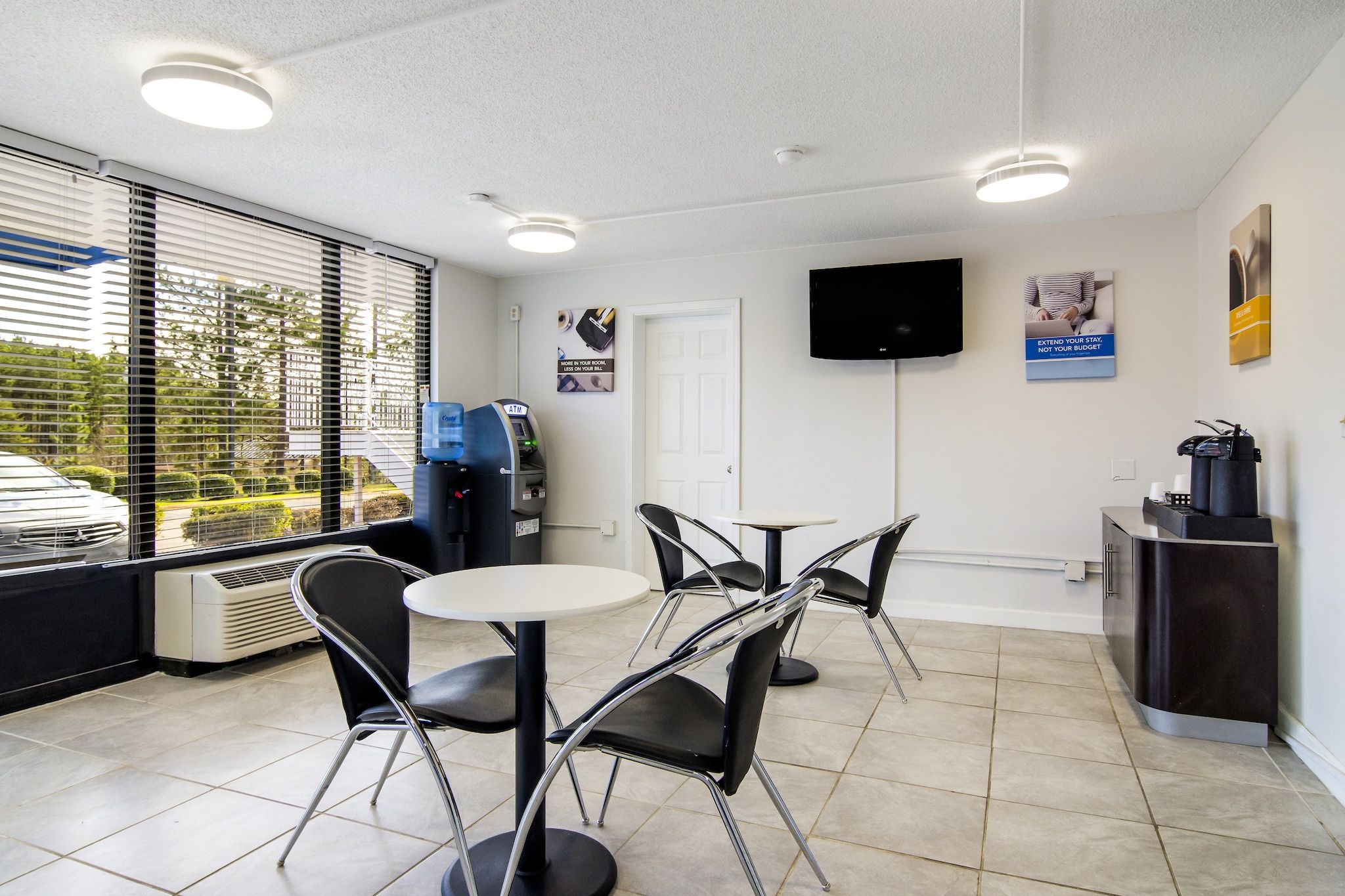 A modern interior with a dining area, a flat-screen TV mounted on the wall, and a view of the outside through large windows.