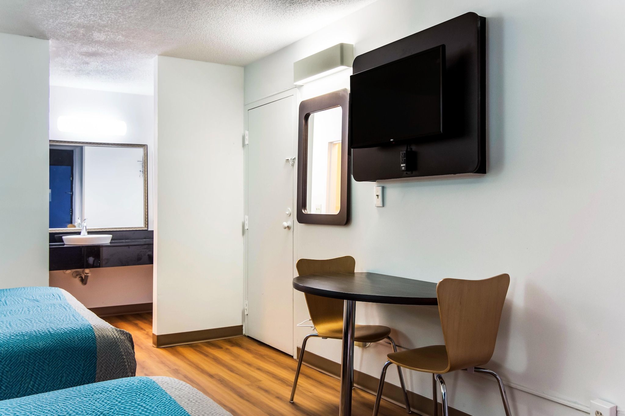 Une chambre d’hôtel avec un lit, un bureau et une chaise, un téléviseur fixé au mur, et une salle de bain visible à travers une porte ouverte.