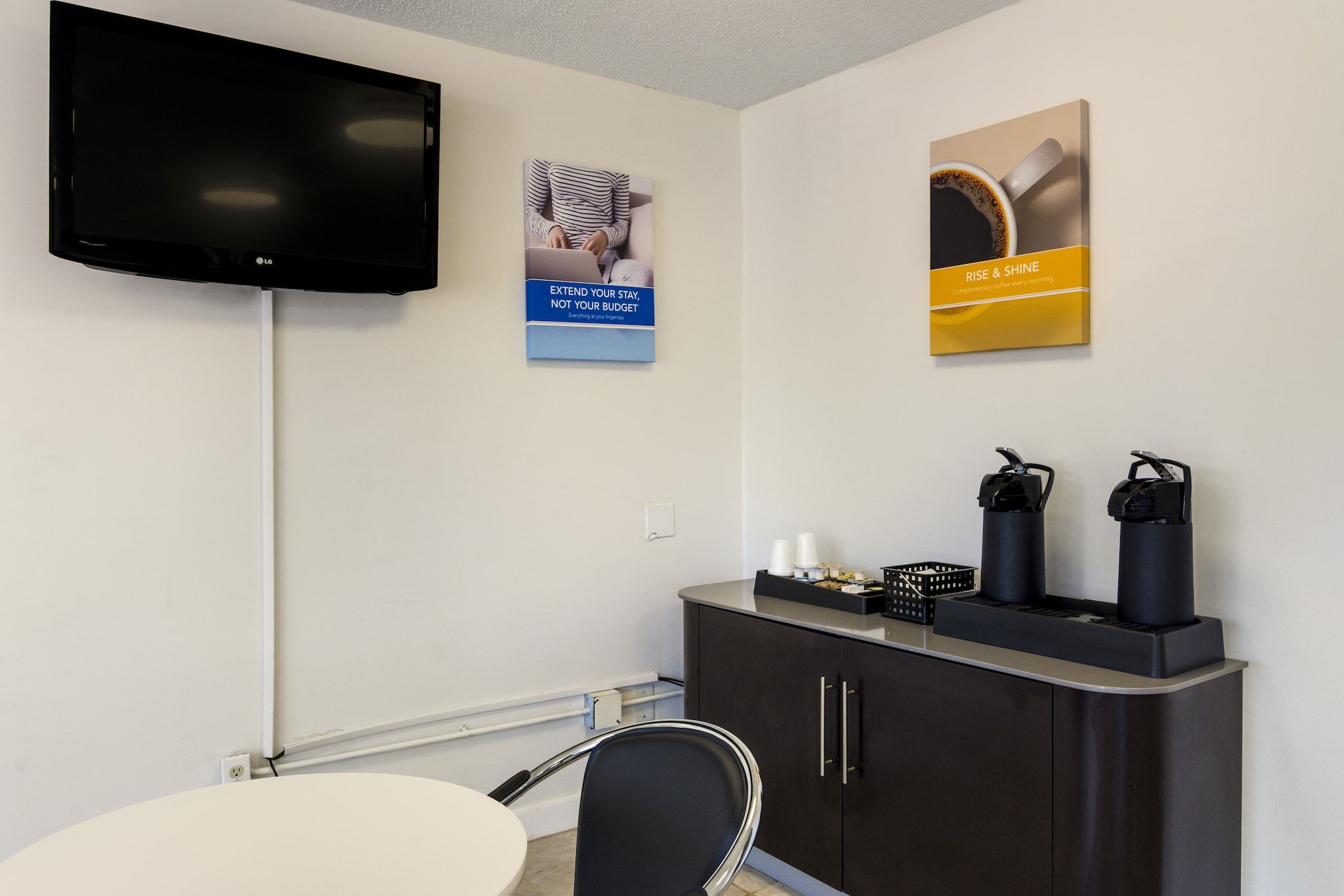 Une chambre d’hôtel équipée d’un téléviseur à écran plat, d’un bureau avec une chaise, d’une machine à café et d’une armoire ornée d’une affiche au mur.