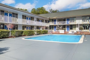 Un motel de dos pisos con piscina, asientos al aire libre y un área cercada.