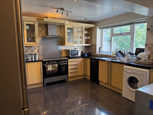 A modern kitchen with a stainless steel range hood, a built-in microwave, a dishwasher, and a washing machine. - Double room upstairs R2 (Woodhouse)