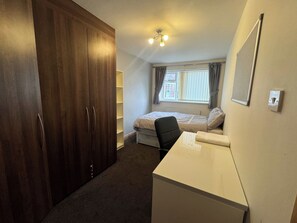 A bedroom with a bed, a desk, a chair, a wardrobe, and a window with curtains. - Double room upstairs R2 (Woodhouse)