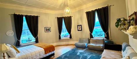 A hotel room with a bed, a sofa, a rug, and a view of a building through the windows.
