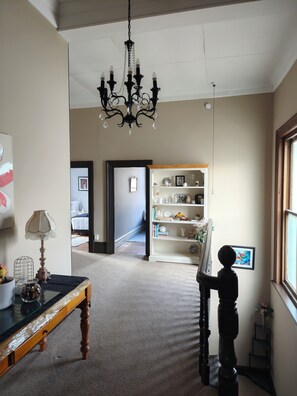 A room with a chandelier, a wooden table with a lamp, a bookshelf, and a painting on the wall. - The Historical Bank house 1 Home Stay (Lawrence)