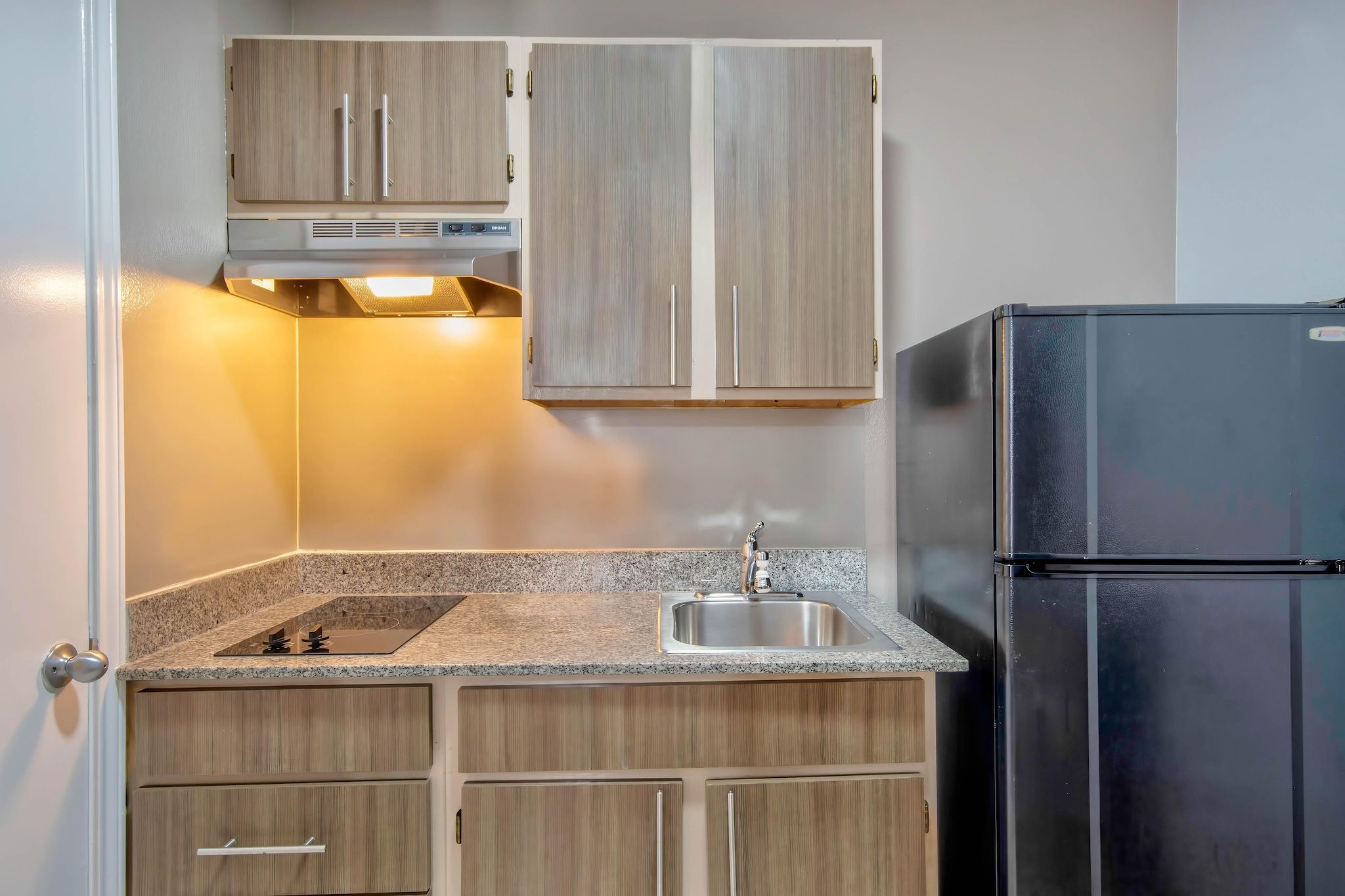 A compact kitchen with wooden cabinets, a stainless steel sink, a black refrigerator, and a built-in oven.