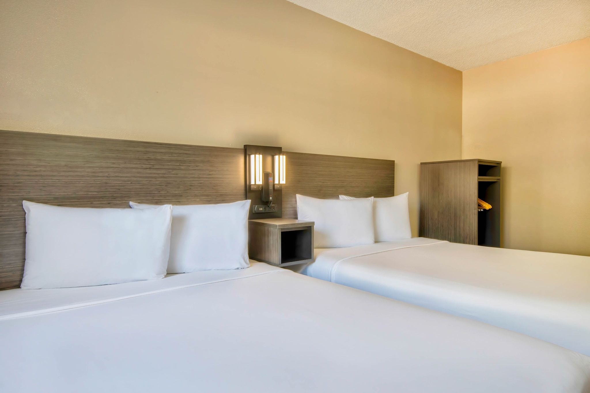A hotel room with two beds, a nightstand, and a wardrobe.