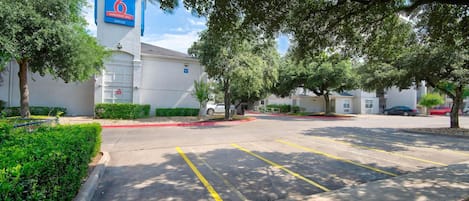 A parking lot with marked spaces, a building with a sign reading 'studio 6 extended stay office', and surrounding greenery.