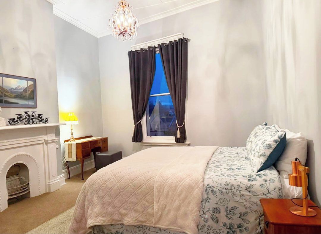 A hotel room with a bed, a desk, a fireplace, and a window with curtains.