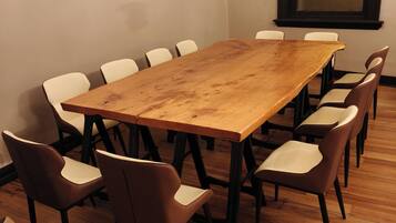 A conference room with a wooden table surrounded by chairs, a window with a view, and a plain wall.