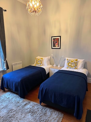 A hotel room with two beds, a chandelier, a framed picture on the wall, and a window with curtains. - The historical Bank house 2 (Lawrence)