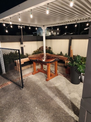 An outdoor patio area with a wooden table and chairs, surrounded by potted plants and a metal fence. - The historical Bank house 2 (Lawrence)