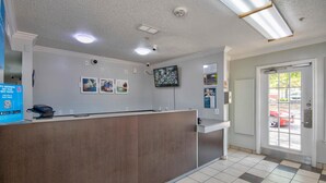 Et receptionområde med disk, loftslamper, et fastmonteret overvågningskamera og en dør med udsigt ud