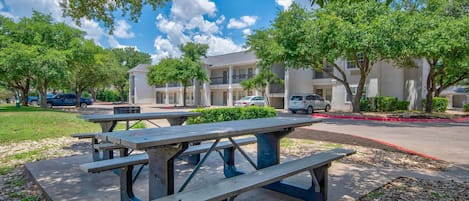 Mesas de picnic al aire libre, un estacionamiento y un edificio con múltiples ventanas y balcones.