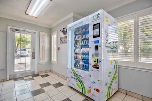 A vending machine with a variety of snacks and drinks, located in a room with a checkered floor and a door leading outside. - 1 Queen Bed | Non-Smoking (Austin)