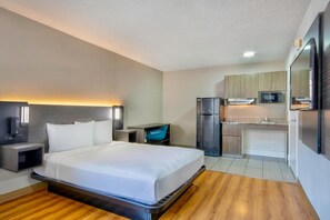 Ein Hotelzimmer mit Bett, Nachttisch, Lampe und einer Küchenzeile inklusive Kühlschrank und Mikrowelle.