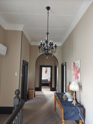 A hallway with a chandelier, a table with a lamp, and a painting on the wall.