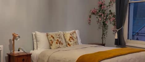 A bedroom with a bed, bedside table, lamp, and a window with curtains.