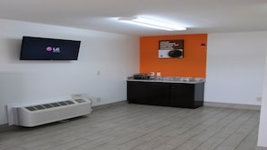 Habitación con televisión de pantalla plana montada en la pared, una kitchenette pequeña con microondas y un aire acondicionado portátil.