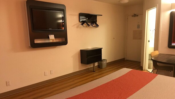 Una habitación de hotel con una cama, un televisor montado en la pared, un perchero y una mesita.