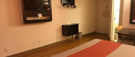 Une chambre d’hôtel avec un lit, un téléviseur fixé au mur, un porte-manteau et une petite table.