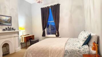 A hotel room with a bed, a desk, a fireplace, and a window with curtains.