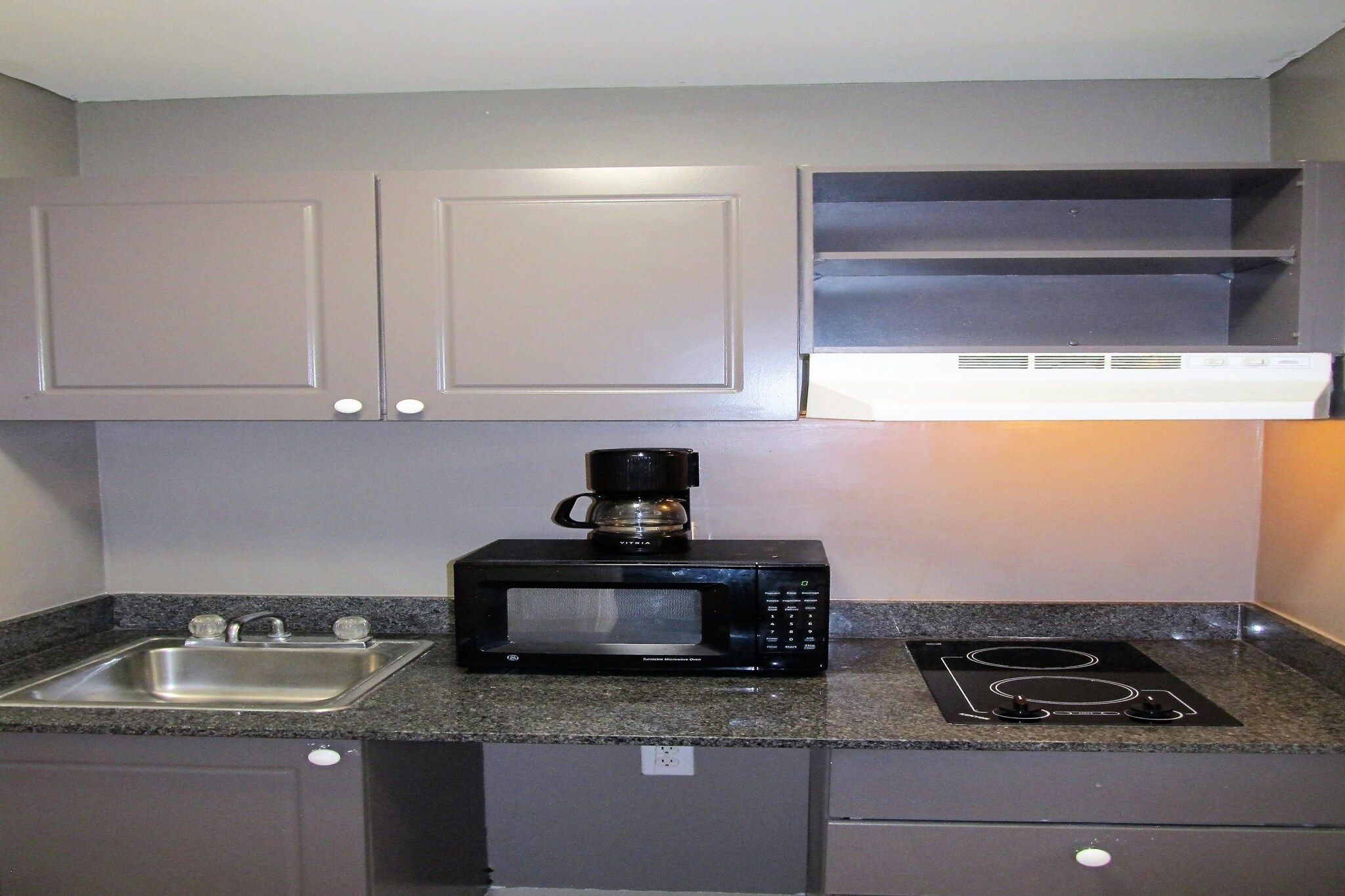 Una kitchenette compacta con microondas integrado, cafetera, pileta y hornalla.