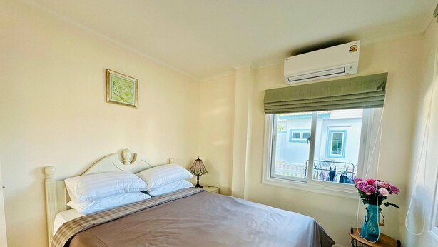 A bedroom with a bed, a window with a view, an air conditioning unit, and a vase with flowers on a nightstand. - The Oasis Pool Villa (Chiang Mai)