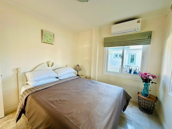 A bedroom with a bed, a window with a view, an air conditioning unit, and a vase with flowers on a nightstand. - The Oasis Pool Villa (Chiang Mai)