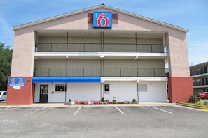 Un motel de dues plantes amb una tenda blava, un cartell d'enregistrament i un pàrquing.