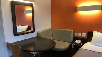 Ein Hotelzimmer mit Bett, kleinem Tisch, Stuhl, Nachttisch mit Telefon und einem an der Wand befestigten Spiegel.