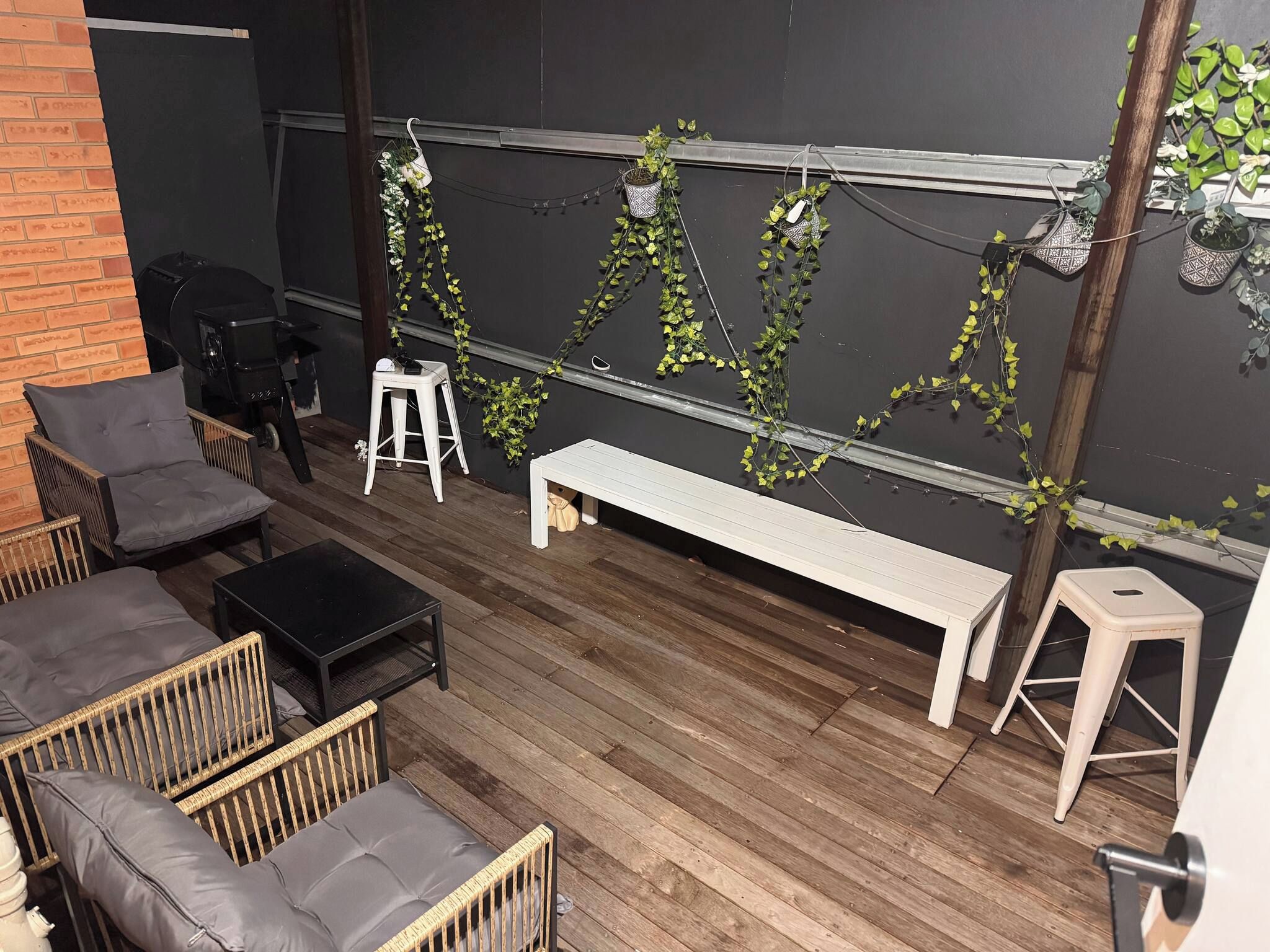 A patio area with a wooden deck, outdoor furniture including a bench and chairs, and a wall adorned with climbing plants.
