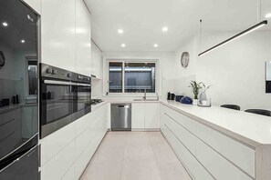 A modern kitchen with white cabinetry, a built-in oven, a stainless steel dishwasher, and a window above the sink.