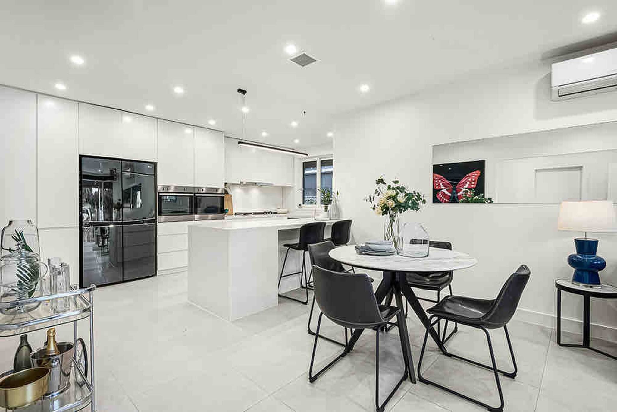 A modern kitchen with white cabinetry, a central island, and a dining area with a round table and chairs.