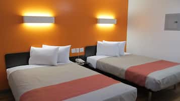 A hotel room with two beds, each with white bedding and a red accent. There are wall-mounted light fixtures above the beds and a telephone on the nightstand.