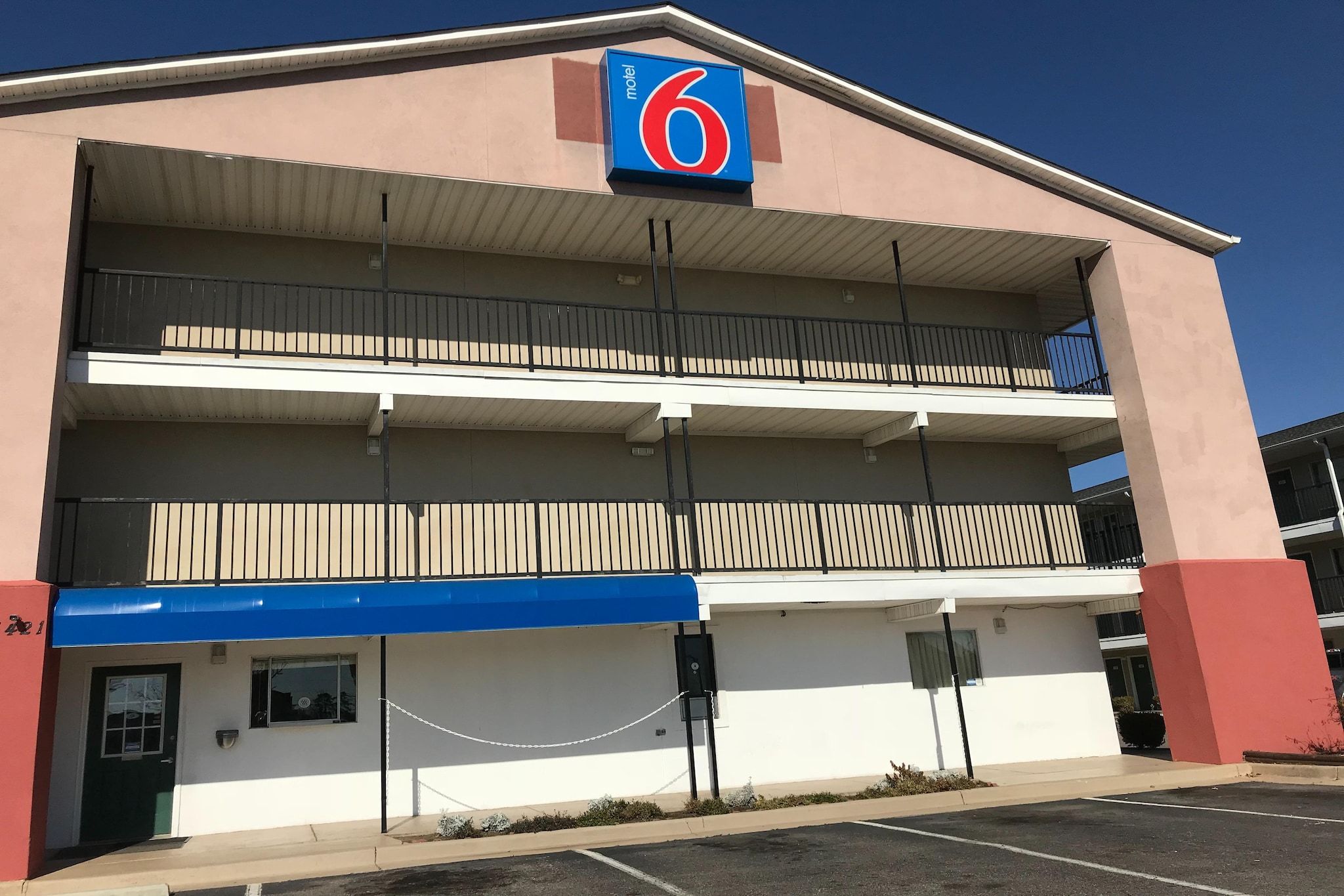 Et motel med et tydeligt skilt med nummer '6', flere balkoner og en parkeringsplads.
