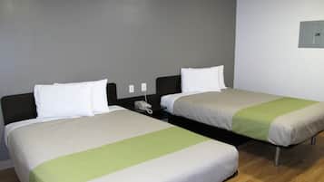 Two single beds with white and green bedding, a bedside table with a phone, and a wall socket.