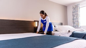 A hotel room with a bed, a nightstand, and a wall-mounted lamp. - Comfort 2 Full Beds | Mini Fridge (Bradenton)