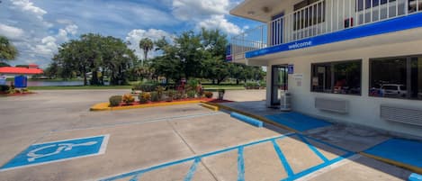 Un edificio con fachada azul y blanca, una rampa que conduce a la entrada y un estacionamiento con plazas reservadas para personas con discapacidad, indicadas en azul.
