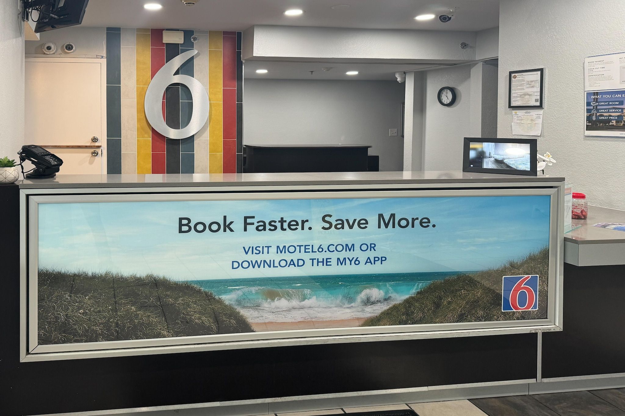 A reception desk with a large sign advertising a booking app, a number '6' sign, and a clock on the wall.