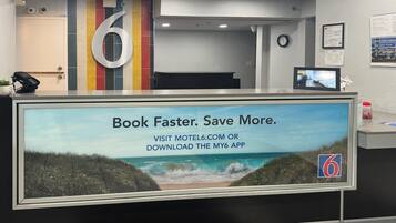 A reception desk with a large sign advertising a booking app, a number '6' sign, and a clock on the wall.