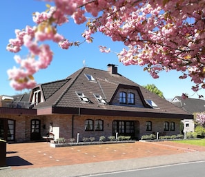 Ein zweistöckiges Haus mit geneigtem Dach, zahlreichen Fenstern und einer Ziegelaußenwand.