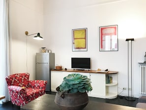 A modern living room with a flat-screen TV, artwork on the wall, a red patterned chair, a potted plant, and a vintage clock on a cabinet. - Casa Marina (Roma)