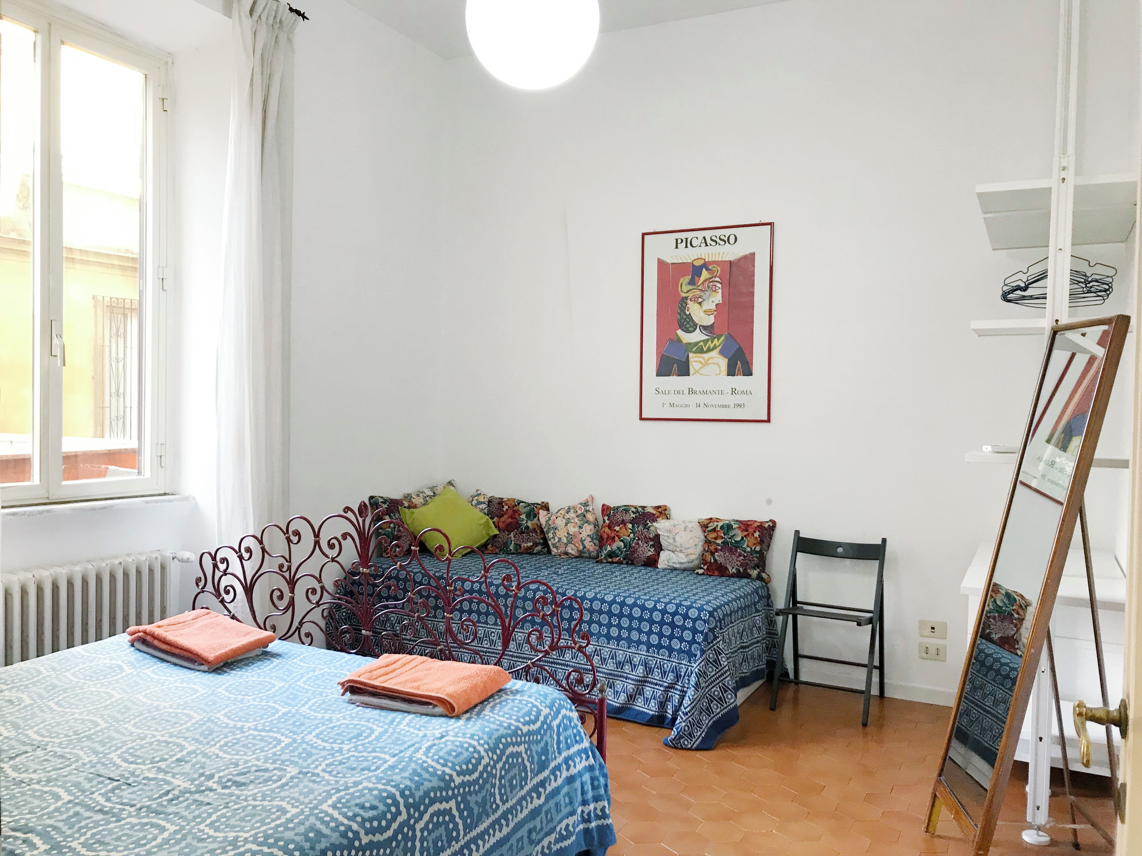 A room with two beds, a radiator, a window with curtains, a poster on the wall, and a mirror leaning against the wall.