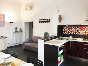 A modern kitchen with a central island, a dining area with a table and chairs, and a living area with a sofa. - Casa Marina (Roma)