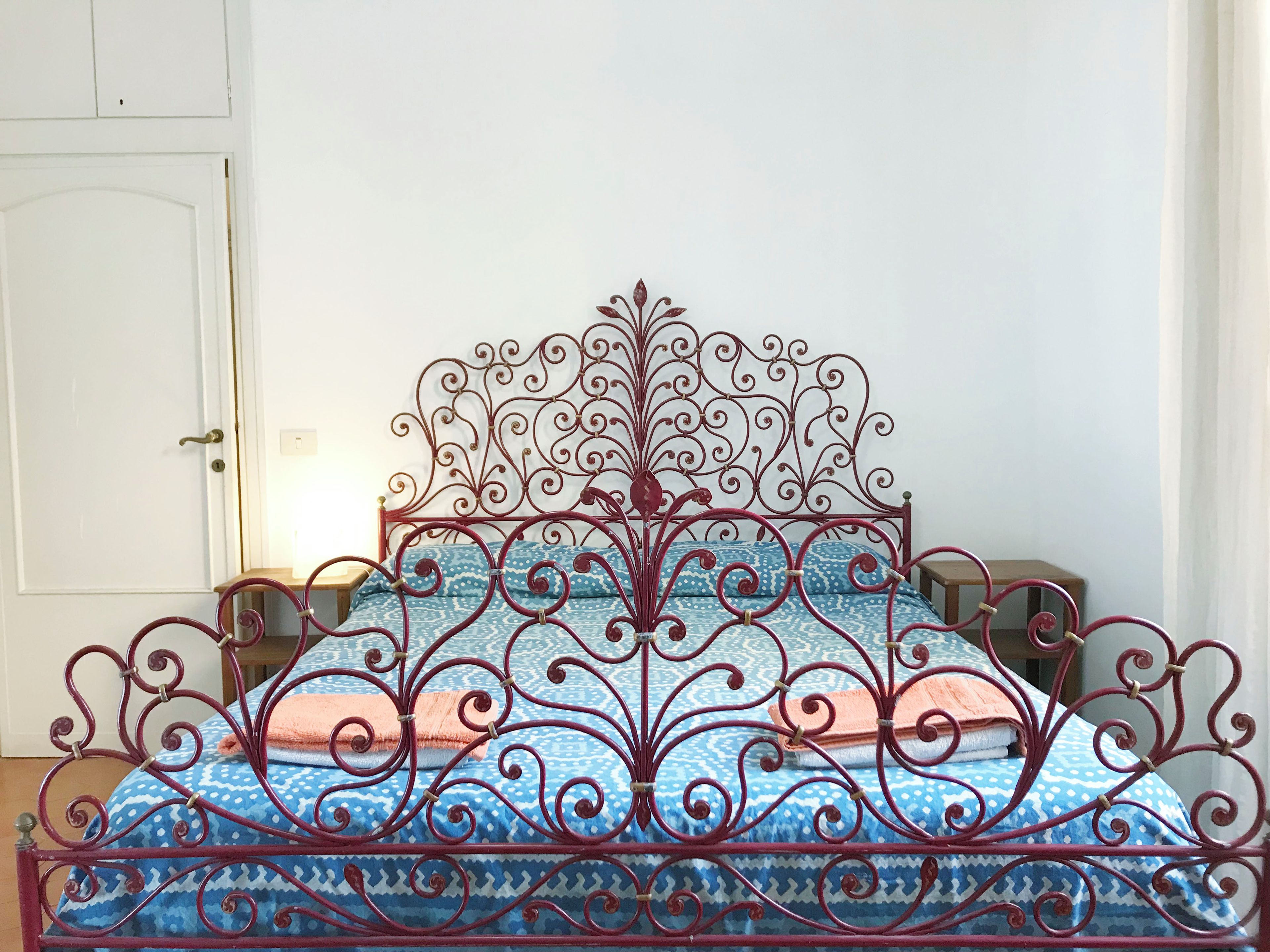 A metal bed frame with intricate designs, a patterned bedspread, and a wooden nightstand.