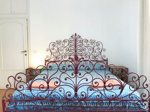 A metal bed frame with intricate designs, a patterned bedspread, and a wooden nightstand. - Casa Marina (Roma)