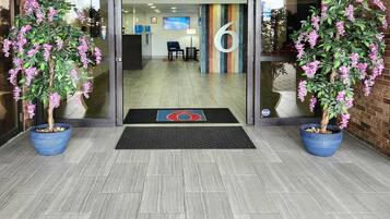 A reception area with a glass door, a number '6' sign, and two potted plants.