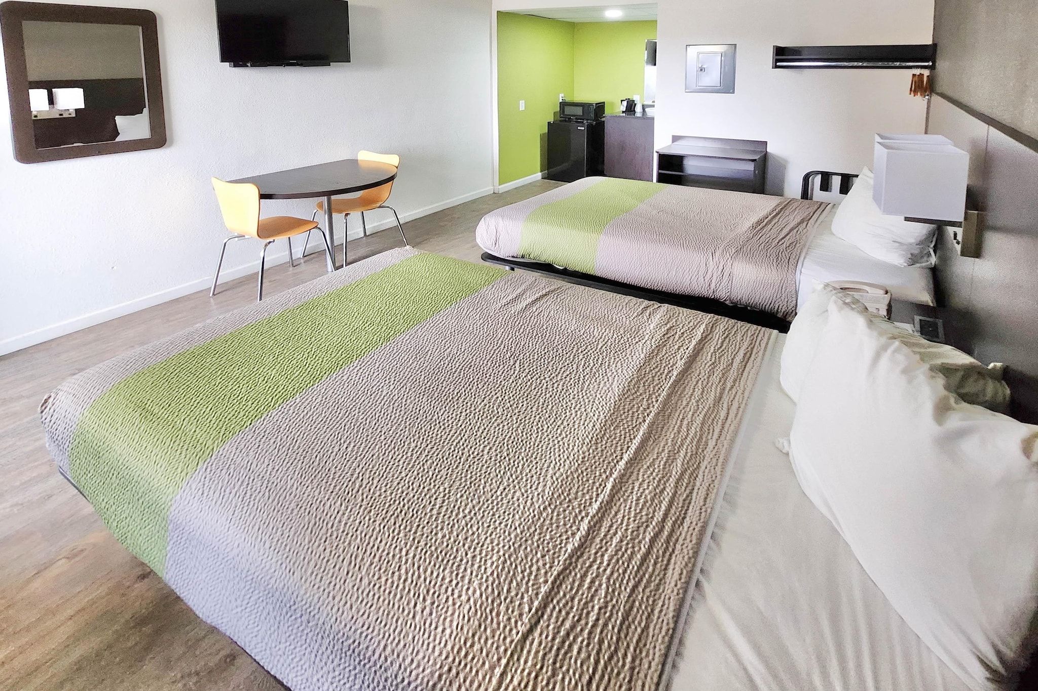 Une chambre d’hôtel avec un lit, un bureau, une chaise, une télévision et un mur vert.