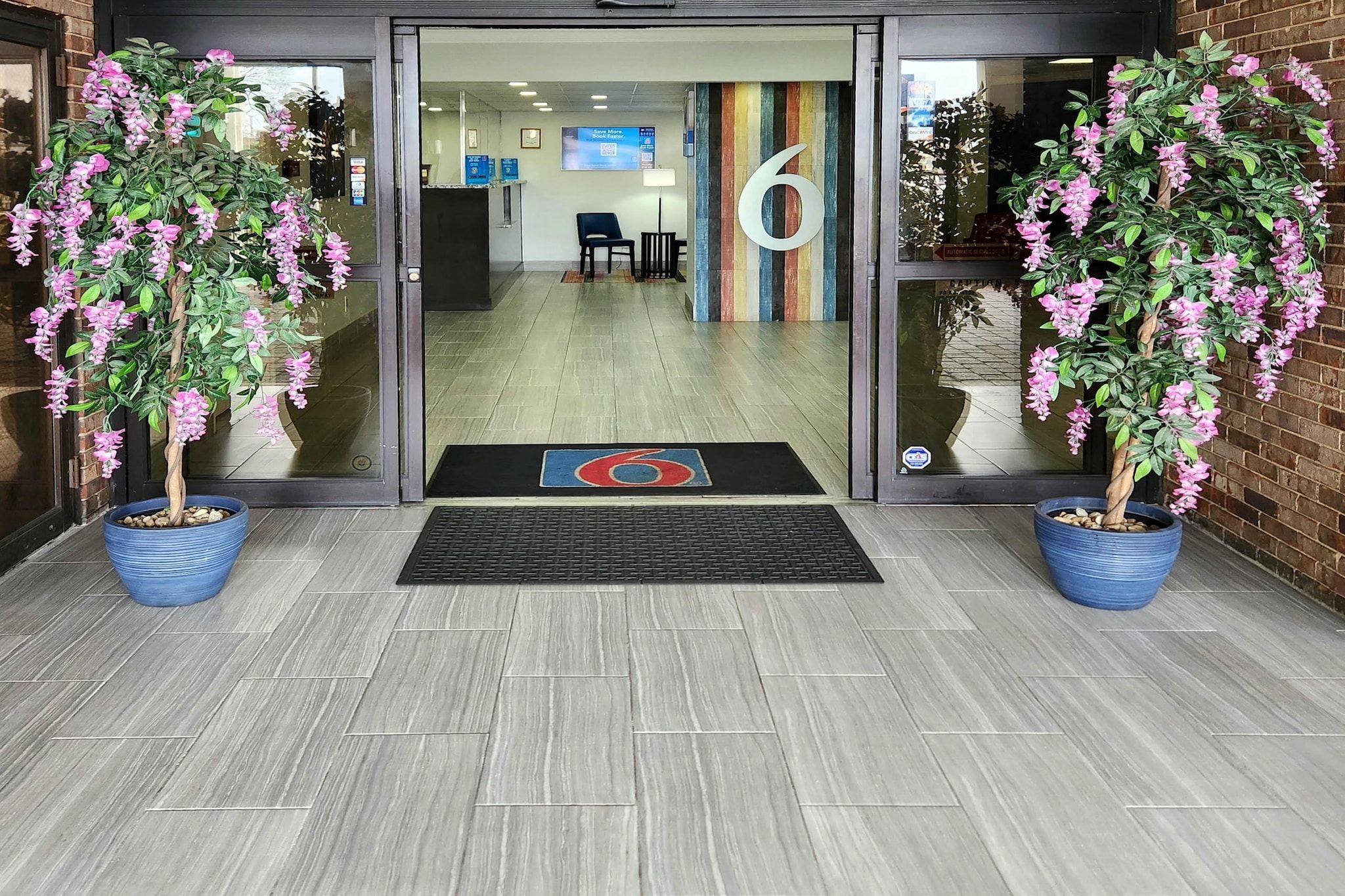 A reception area with a glass door, a number '6' sign, and two potted plants.